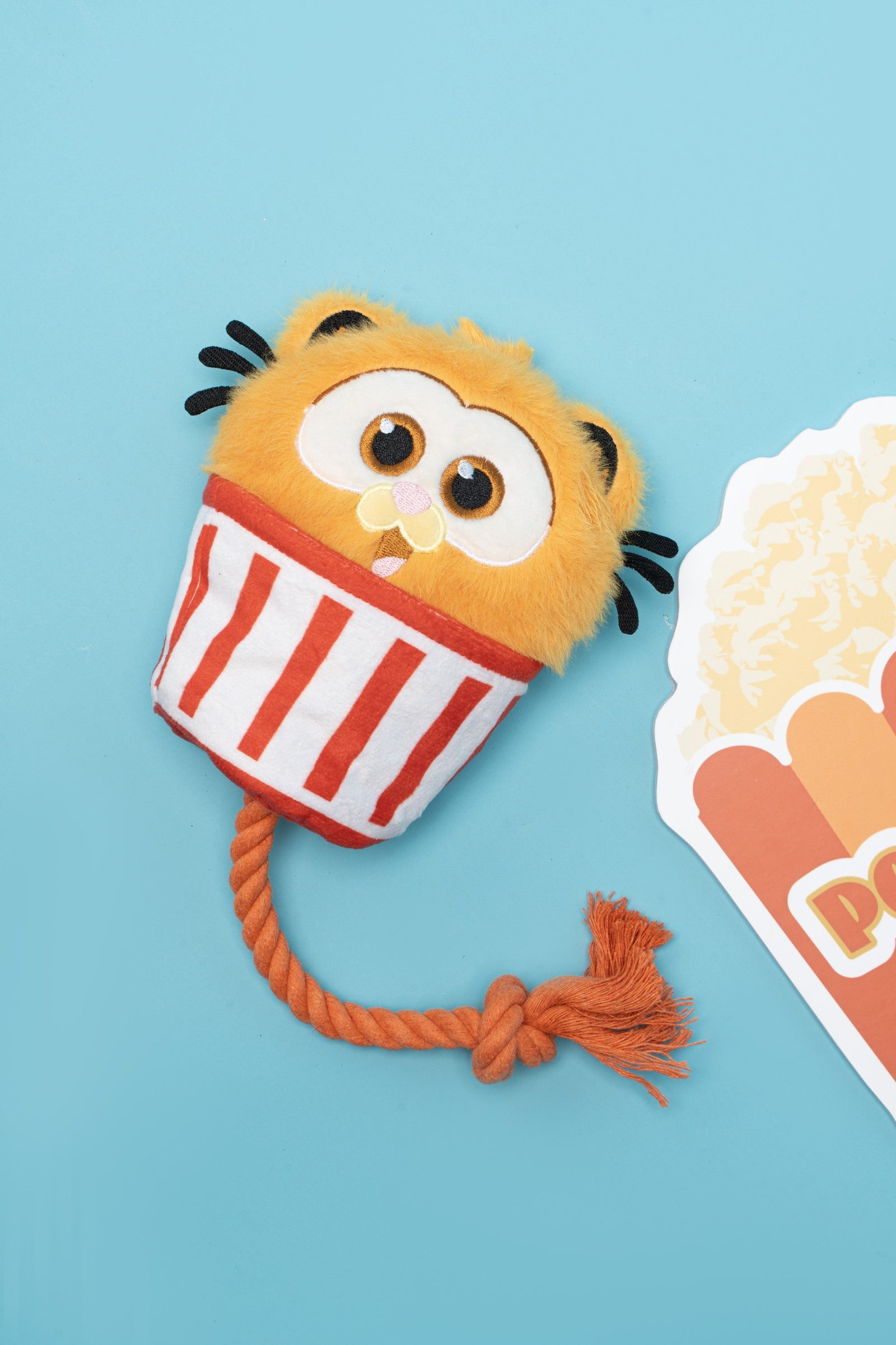 Garfield popcorn-cup plush toy with an orange knotted rope on a blue background