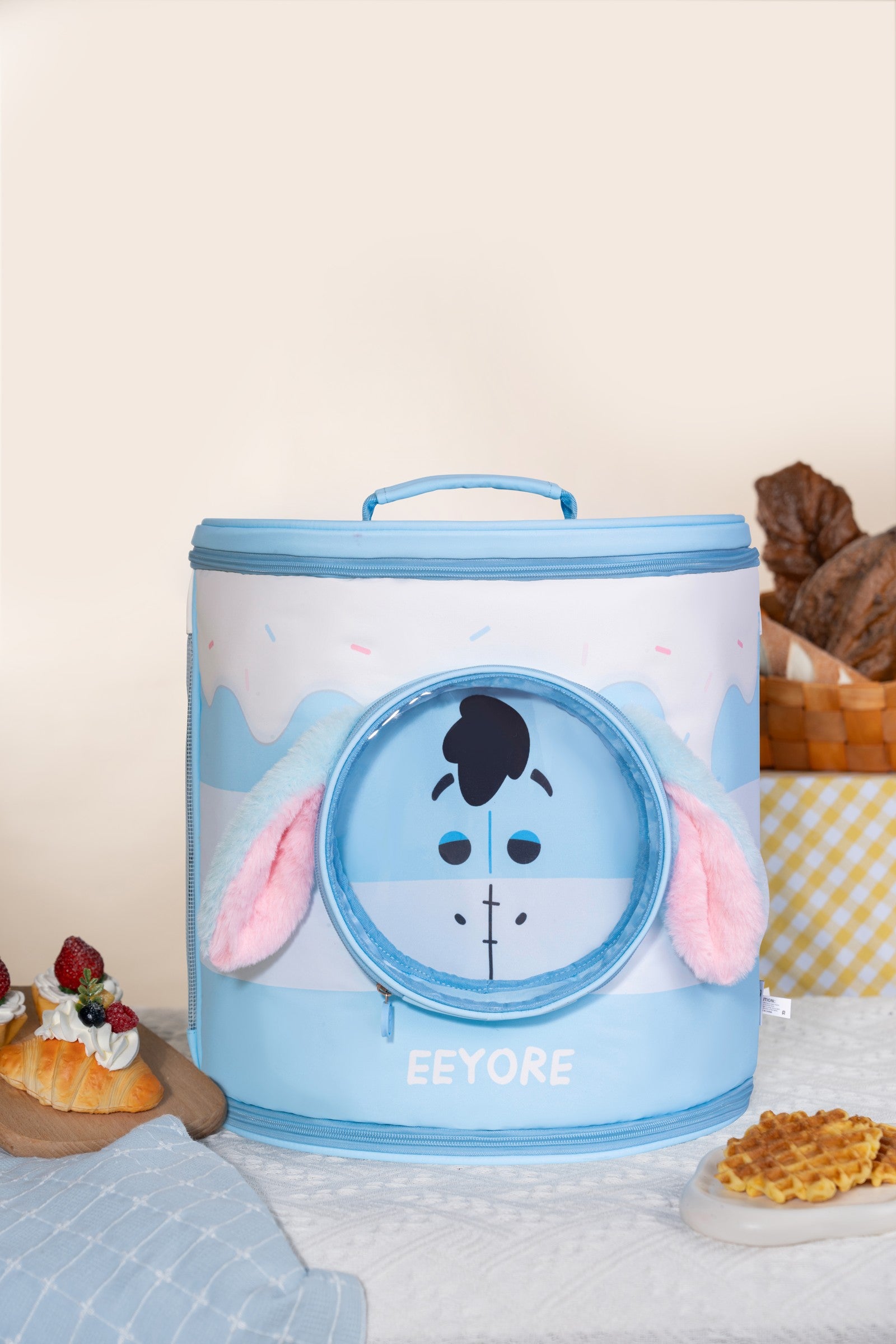 Blue Eeyore backpack-style pet carrier with long ears in a bakery-inspired still-life