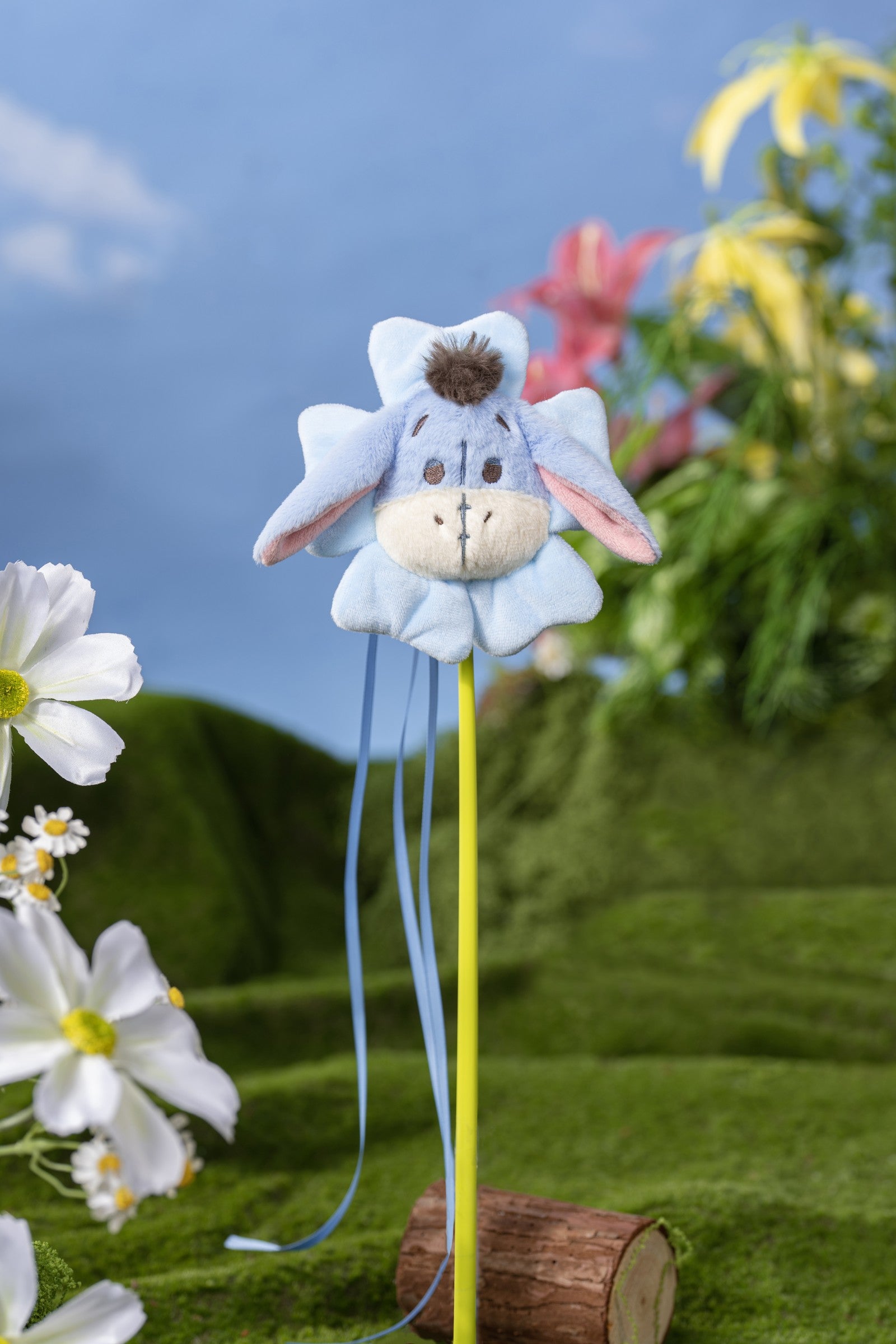 Eeyore character wand toy photographed among flowers and green plants